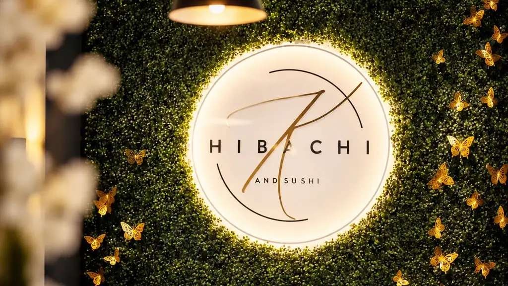 The Hibachi K and Sushi logo, lit from behind, on a boxwood wall hung with gold butterflies inside the restaurant
